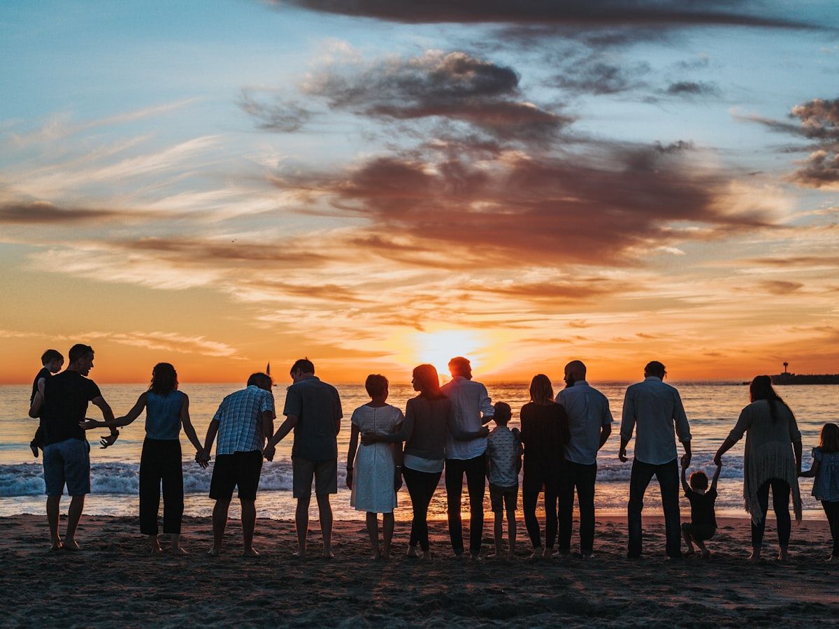 A multi-generation family standing together on the beach at sunset